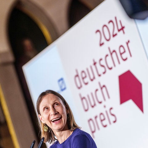 Frau lacht, hinter ihr hängt ein Schild mit der Aufschrift "Deutscher Buchpreis"