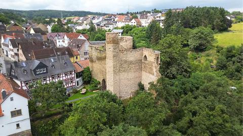 Burgruine auf einem Steilhang zwischen Häusern, nebendran ein großes Fachwerkhaus