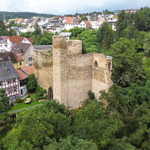 Burgruine auf einem Steilhang zwischen Häusern, nebendran ein großes Fachwerkhaus