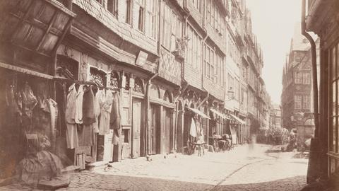 Schwarz-weiß-Foto einer Gasse, die von Fachwerkhäusern gesäumt ist.