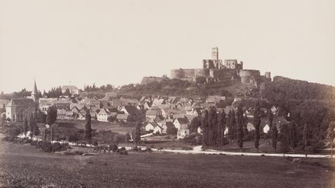 Schwarz-Weiß-Foto, es zeigt einen Hügel, auf dem eine Burg liegt. Am Fuß des Hügels liegt eine Siedlung.