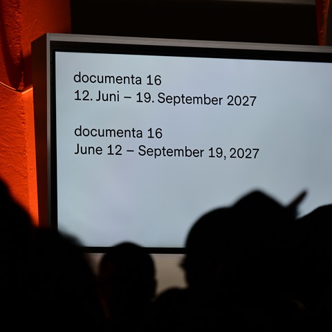 Auf einem Monitor an der Wand vom Friz ist anlässlich der Schließung der documenta fifteen der Termin für die documenta 16 genannt, die vom 12. Juni 2027 bis 19.September 2027 dauern soll.