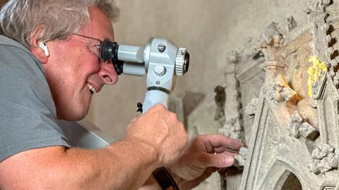 Restaurator Matthias Steyer untersucht die verzierten Grabplatten mit einer Mikroskop-Brille bei Scheinwerferlicht.