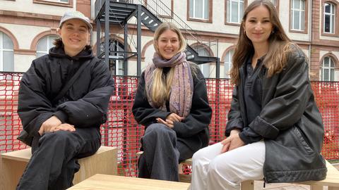 Drei junge Frauen sitzen auf Holzmöbeln