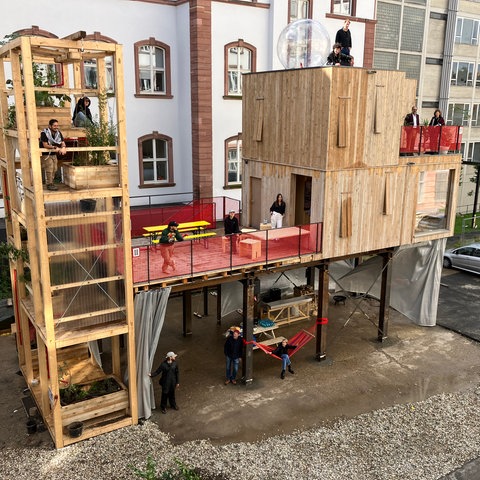 Bauwerk auf Holz mit verschiedenen Ebenen, darin Menschen