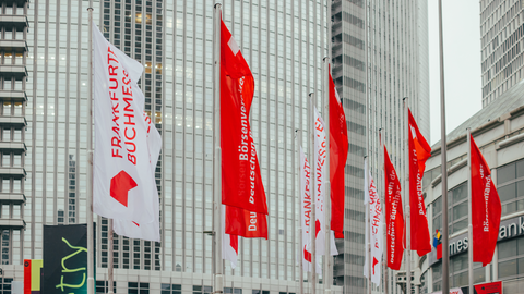 Vor der Frankfurter Messehalle wehen mehrere rote und weiße Fahnen mit der Aufschrift "Frankfurter Buchmesse" und "Börsenverein des deutschen Buchhandels".