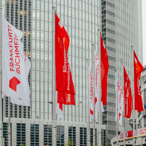 Vor der Frankfurter Messehalle wehen mehrere rote und weiße Fahnen mit der Aufschrift "Frankfurter Buchmesse" und "Börsenverein des deutschen Buchhandels".