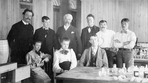 Schwarz-Weiß-Fotografie von neun Menschen in einem Labor. In der unteren Reihe mittig sitzt eine Frau.