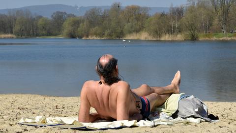 Ein Mann in Badehose liegt auf einem Handtuch im Sand an der Fuldaaue in Kassel.