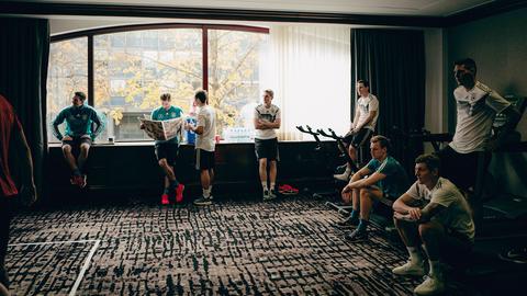 Männer in Fußball-Trikots stehen und sitzen wartend in einem Konferenzraum.