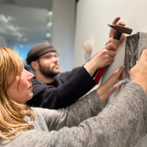 Zwei Menschen hängen ein Bild an die Wand