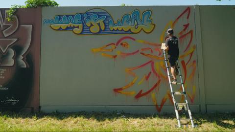 Mann auf einer Leiter sprayt Graffiti auf eine Wand