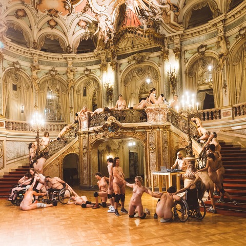 Nackte Menschen, einige im Rollstuhl, im barocken Foyer des Staatstheaters Wiesbaden.