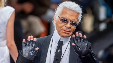 Modedesigner Karl Lagerfeld hebt abwehrend seine Hände. Er trägt Lederhandschuhe ohne Finger.