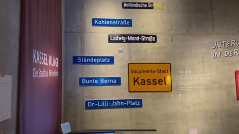 Ein Kasseler Ortsschild mit Straßenschildern an einer Wand