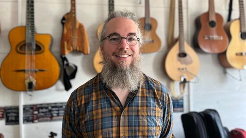 Gitarrenlehrer Jan Jansohn steht in seinem Arbeitszimmer, im Hintergrund sieht man diverse Gitarren an der Wand hängen.