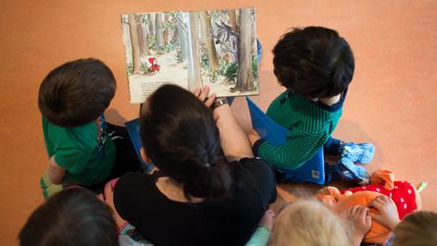 Eine Frau hält ein Bilderbuch in der Hand und ist umringt von fünf Kindern. Fotografiert von oben.