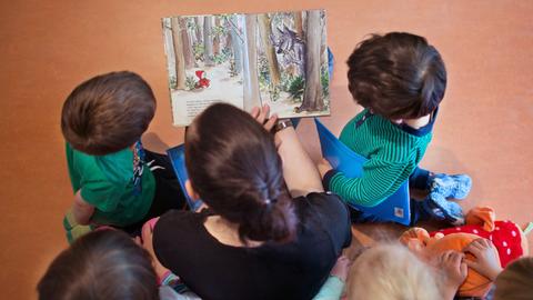 Eine Frau hält ein Bilderbuch in der Hand und ist umringt von fünf Kindern. Fotografiert von oben.