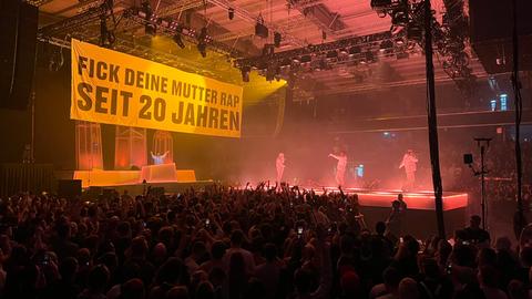 Über der Bühne in der Nordhessen-Arena ist ein großes Banner zu sehen. Darauf steht "Fick Deine Mutter Rap seit 20 Jahren".