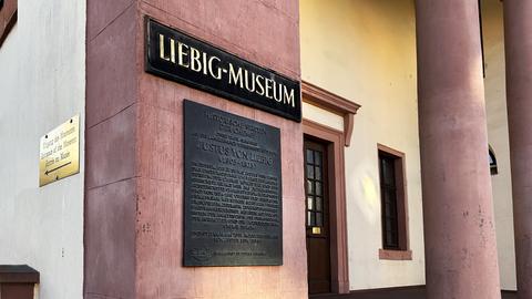 Eingang in ein historisches Gebäude. An der Wand Schild mit der goldenen Aufschrift "Liebig-Museum". Darunter eine graue Texttafel.