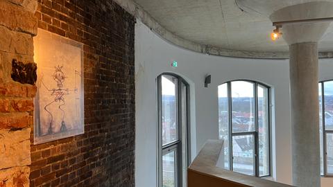 Ein Innenraum mit einer rote Backsteinwand und einem weißen Erker mit großen Fensterscheiben. An der Decke sind Wasserschäden zu erkennen.