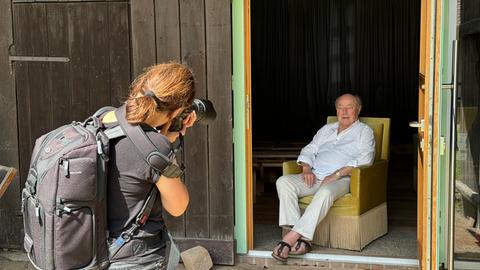 Jürgen Flügge sitzt auf einem Sessel, Petra Arnold fotografiert ihn. 