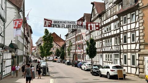 In einer Straße hängt zwischen den Häusern ein großes Banner mit der Aufschrift "Open Flair-Festival".