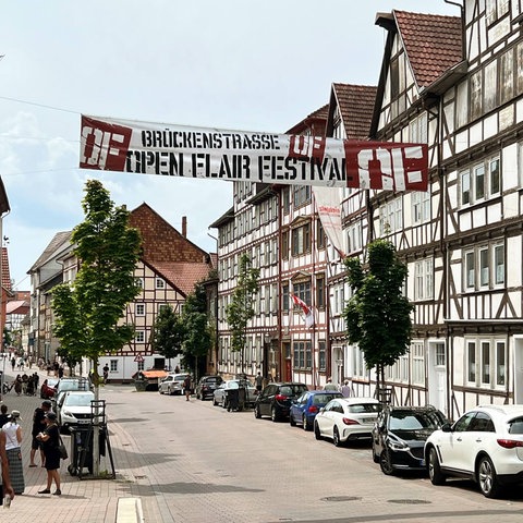 In einer Straße hängt zwischen den Häusern ein großes Banner mit der Aufschrift "Open Flair-Festival".