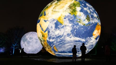 Ein zehn Meter hoher Globus steht vor einem kleineren Mond. 