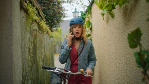 Anke Engelke hält in der einen Hand ein Handy, in der anderen ein Fahrrad.