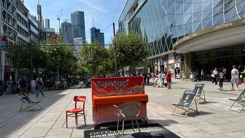 Auf der Frankfurter Zeil steht ein rot lackiertes Piano. Rechts am Bildrand ist das Shoppingcenter MyZeil zu sehen.