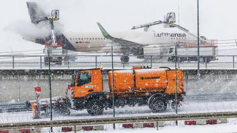 Ein Flugzeug am Frankfurter Flughafen wird bei Schnee und Glätte enteist, davor fährt ein Winterdienstfahrzeug.