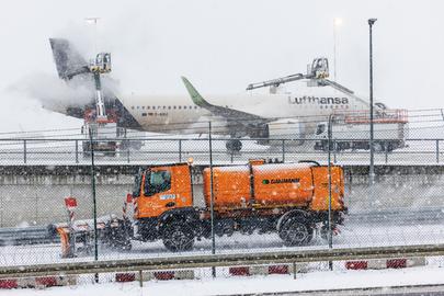 Ein Flugzeug am Frankfurter Flughafen wird bei Schnee und Glätte enteist, davor fährt ein Winterdienstfahrzeug.