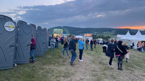 Mehrere Menschen warten vor Dixie-Klos am Rande der Konzertwiese.