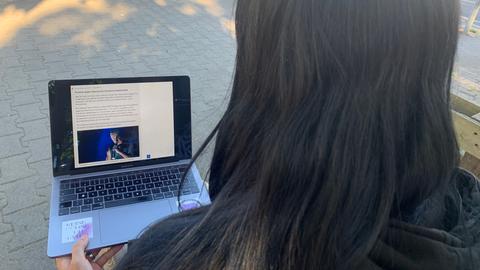 Eine Person mit langen, dunklen Haaren blickt auf einen Laptop mit dem Bild von Till Lindemann