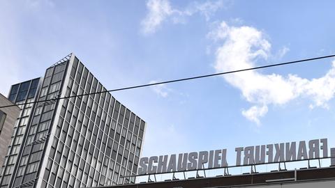 Das Bild zeigt den Willy-Brandt-Platz in Frankfurt mit dem Schauspiel. Zu sehen sind angeschnittene Hochhäuser links im Bild sowie der Schriftzug "Schauspiel Frankfurt" auf dem Dach des Theatergebäudes. Dabei ist das Wort Frankfurt in falscher Reihenfolge geschrieben, sodass es wie gespiegelt aussieht. Darüber ist blauer Himmel zu sehen.