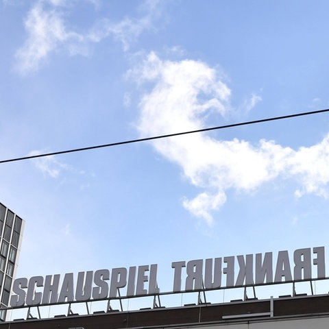 Das Bild zeigt den Willy-Brandt-Platz in Frankfurt mit dem Schauspiel. Zu sehen sind angeschnittene Hochhäuser links im Bild sowie der Schriftzug "Schauspiel Frankfurt" auf dem Dach des Theatergebäudes. Dabei ist das Wort Frankfurt in falscher Reihenfolge geschrieben, sodass es wie gespiegelt aussieht. Darüber ist blauer Himmel zu sehen.