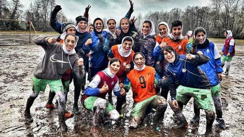 Schlammverschmierte Frauen jubeln auf einem matschigen Fußballplatz