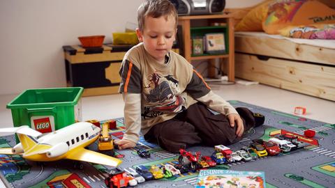 Ein Junge mit Autos auf einem Straßen-Teppich im Kinderzimmer. 