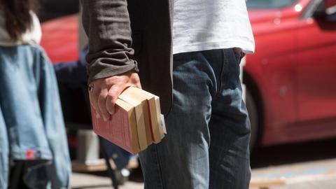 Ein Mann trägt mehrere Bücher in einer Hand