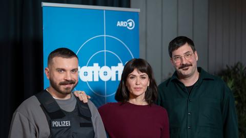 Drei Menschen vor einem Aufsteller mit Tatort-Logo, einer trägt einen Pulli mit Aufschrift "Polizei" und eine schussichere Weste