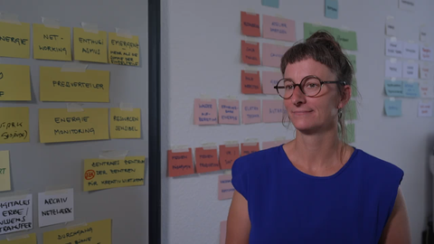 Die Projektkoordinatorin Anne Walther steht vor vielen Post-Its auf einer Wand und schaut an der Kamera vorbei