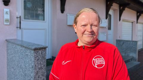 Eine Frau steht vor einem Haus und blickt in die Kamera.