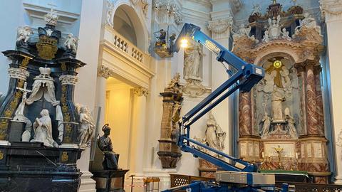 Ein Mann steht auf einer Hebebühne im Fuldaer Dom reinigt Wände und Skulpturen.