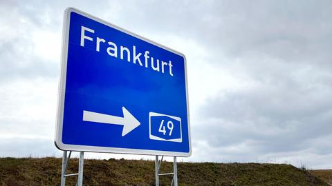 Foto eines großen, blauen Schildes mit der Aufschrift "Frankfurt","49" und einem Pfeil, das an einer Autobahn steht.