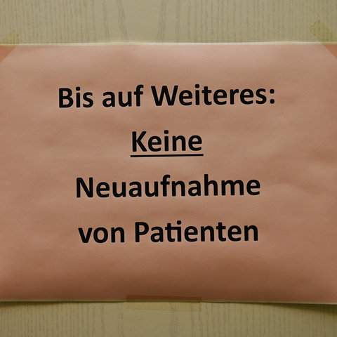 Auf eine Tür ist ein Blatt geklebt mit der Aufschrift: "Bis auf Weiteres: Keine Neuaufnahmen von Patienten"