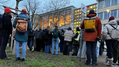 Menschen stehen vor einem beleuchteten Gebäude, auf einem Plakat auf dem Boden steht "Schulverweis für Rechtsextreme".