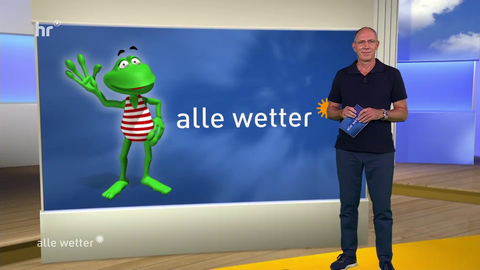 Moderator Thomas Ranft steht vor einem Bildschirm, auf dem Wetterfrosch Fridolin zu sehen ist.