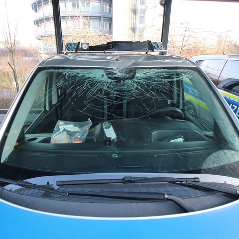 Ein Polizeiwagen mit zerstörter Frontscheibe und demoliertem Dach-Blaulicht. 