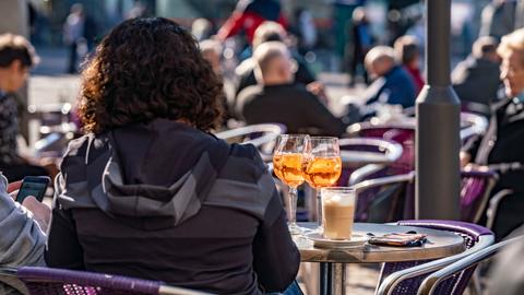 Besucher eines Straßencafes in der Innenstadt von Darmstadt im Sonnenschein, im Vordergrund eine Frau von hinten vor zwei Drinks und einem Kaffee